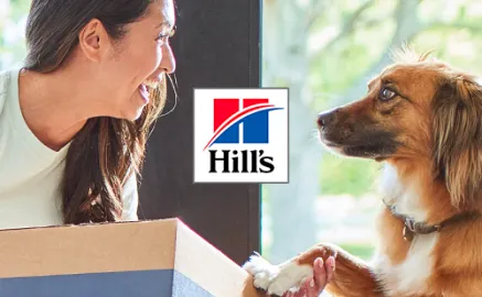 A pet owner and a dog sitting beside Hill's Pet food packaging